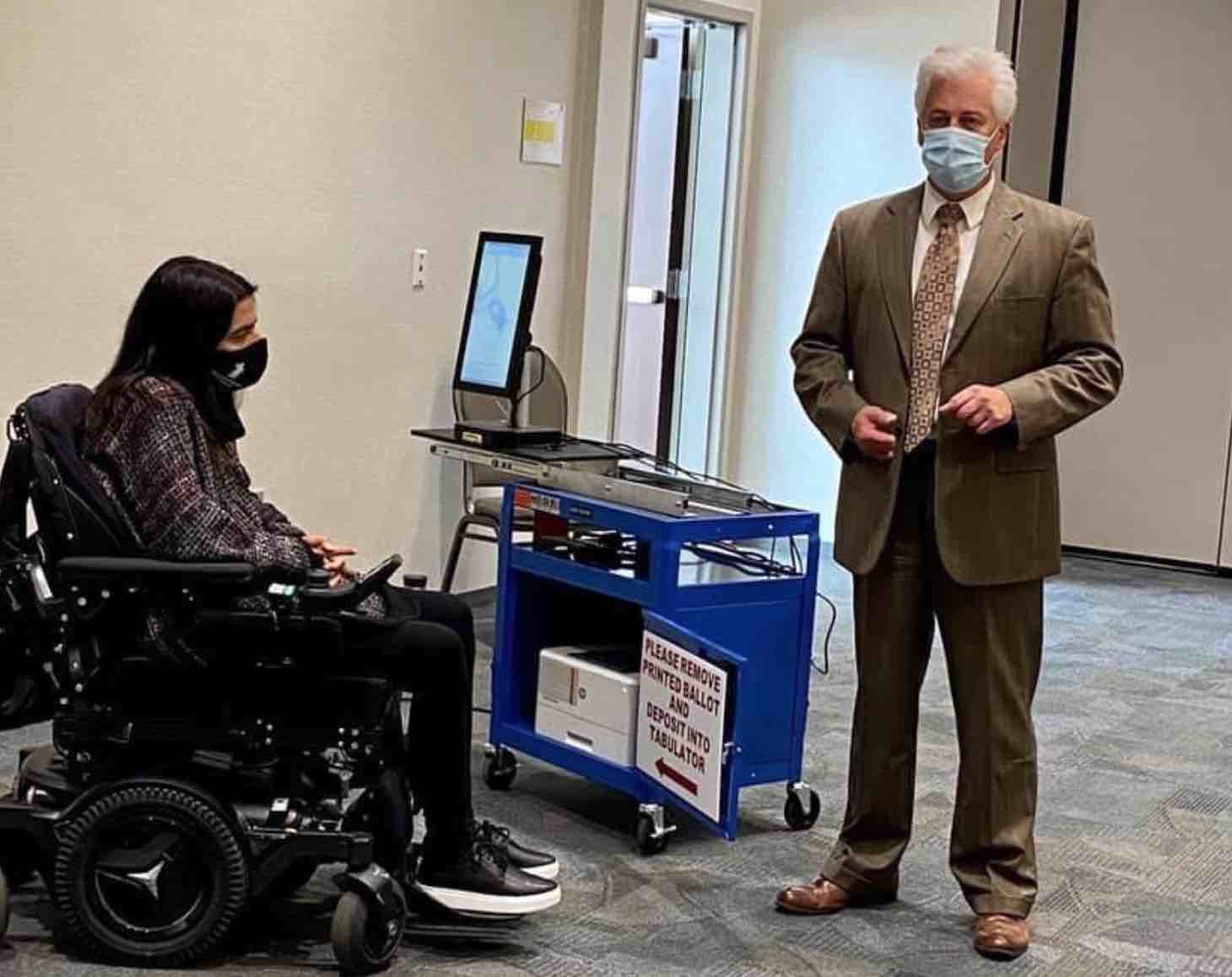 picture of woman using wheelchair and man standing at a voting station